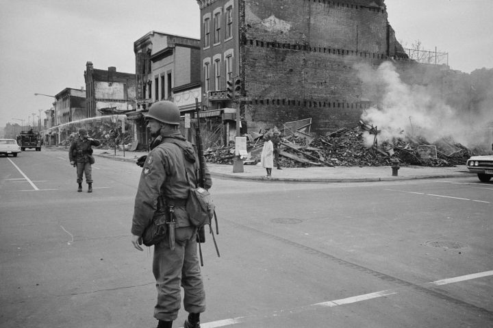 Soldier standing guard in a Washington, D.C., street with the ruins of buildings that were destroyed during the riots that followed the assassination of Martin Luther King Jr., 8 April 1968. Photographer: Warren K Leffler.