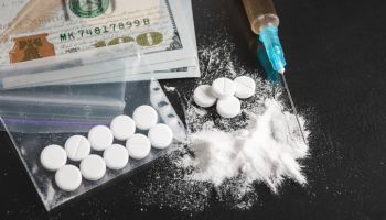 Drugs on dark background, cocaine or heroin white powder, white pills, syringe with a dose and us dollar cash. Drug abuse and addiction concept