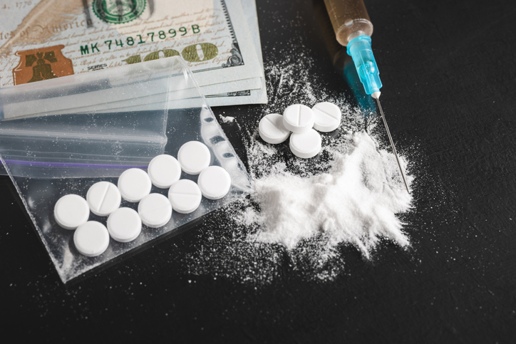 Drugs on dark background, cocaine or heroin white powder, white pills, syringe with a dose and us dollar cash. Drug abuse and addiction concept