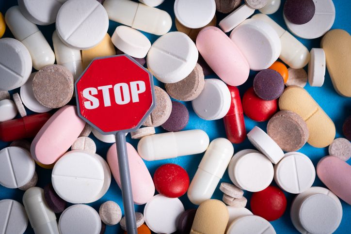 Red stop sign among different pills and capsules on blue background, conceptual image.