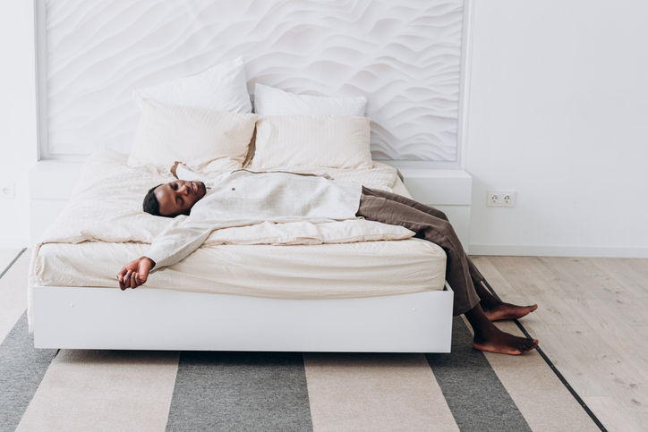 African American man lies spread out on neatly made bed in modern bedroom, enjoying moment of relaxation and comfort.
