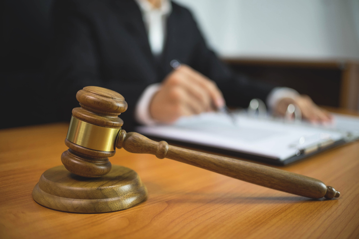 Close-Up Of Gavel With Judge In Background On Table